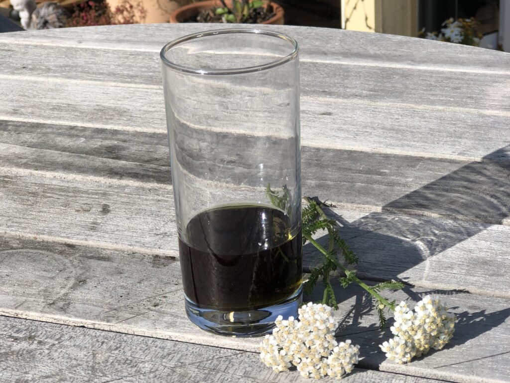 Tinktur av rölleka i ett glas som står på ett grått bord.