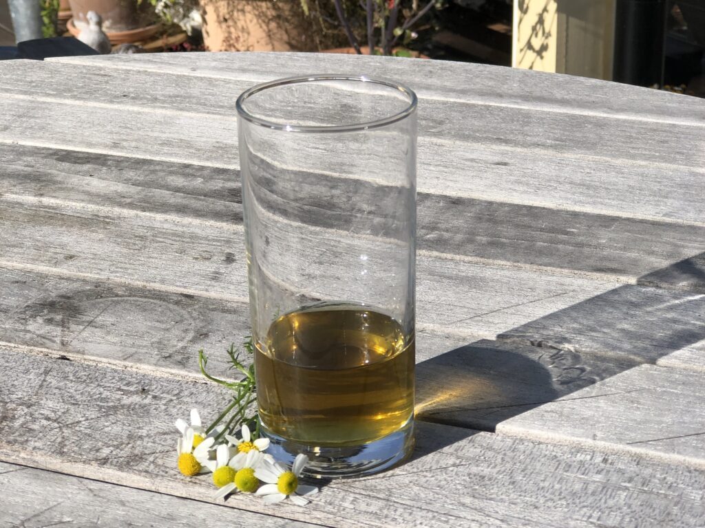 Guldgul tinktur på kamomill i ett glas som står på ett grått bord.